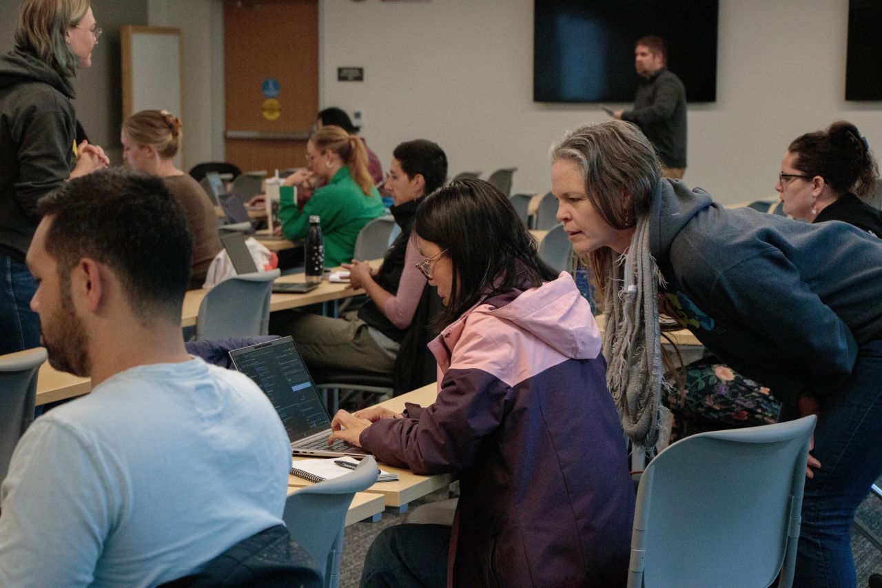 Workshop participants perform an activity on their laptops while instructors walk around the room.